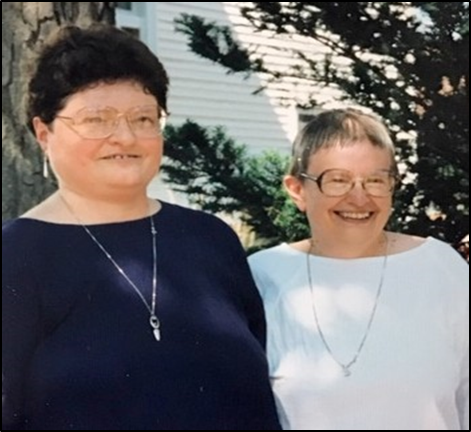Two smiling women standing side by side outdoors.