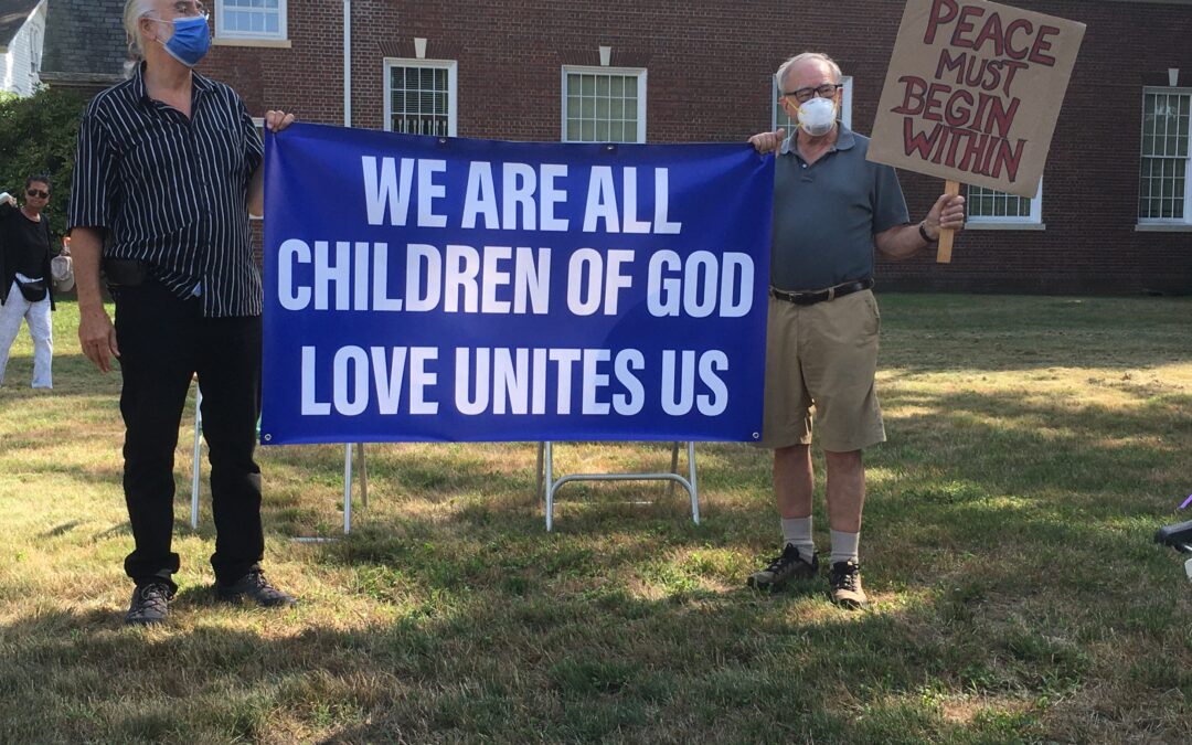 Two men holding a sign thta says "We are all children of God. Love unites us"