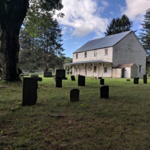 Historic wooden building viewed from a cemetery with weathered headstones.