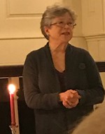 A woman speaking indoors with a lit candle in the foreground.